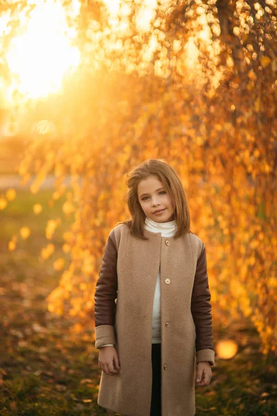 Een tienermeisje staat met een vacht op de achtergrond van de gouden boom. Gele en oranje kleuren van de herfst — Stockfoto