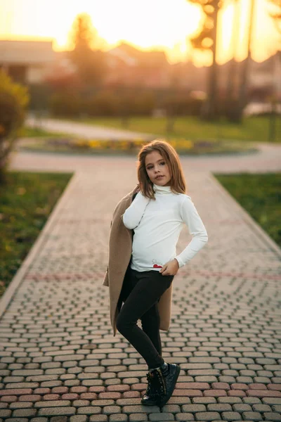 Маленькая девочка гуляет в парке золотой осенью. Она держит пальто и позирует фотографу. — стоковое фото