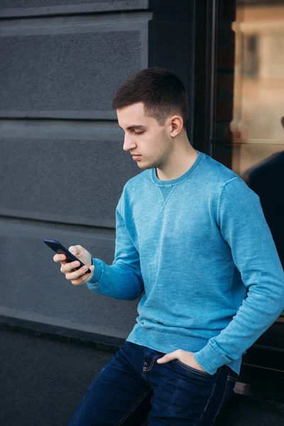 Young man is using the phone on the street. Handsome guy stand in front of window — Stock Photo, Image