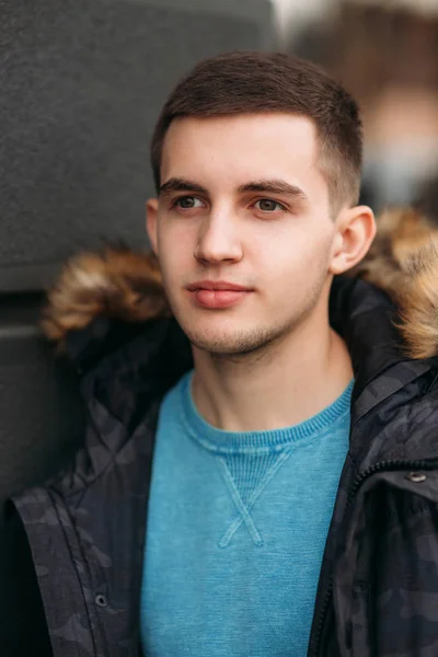 Retrato de homem jovem em uma jaqueta cinza. Ele está parado na rua e posando para um fotógrafo — Fotografia de Stock