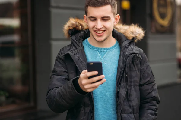 Hombre con una chaqueta gris está de pie afuera y usando un teléfono — Foto de Stock