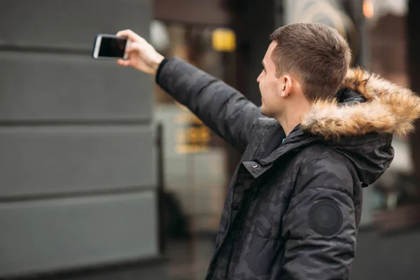 L'uomo in giacca grigia è in piedi fuori con un telefono e fare selfie — Foto Stock