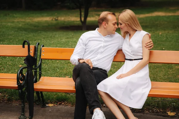 Mooie paar zit op de Bank in het park. Blonde haren man en vrouw besteden tijd togerther. Zij zwarte paraplu. Achtergrond van groen gras — Stockfoto