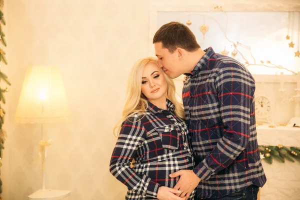 Happy couple in holiday spirit showing affection for one another. Dressed in plaid clothes. Gentle pregnant woman.