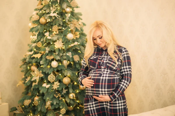 Eine schöne schwangere blonde Mädchen schmückt einen Weihnachtsbaum mit schönen Spielzeug. Weihnachtsstimmung — Stockfoto