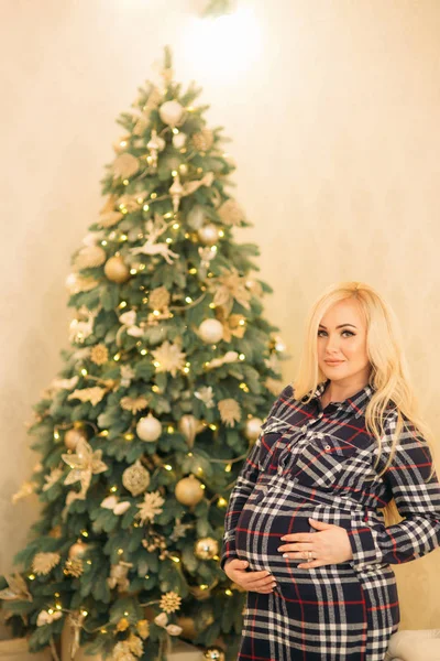 Una hermosa chica rubia embarazada decora un árbol de Navidad con hermosos juguetes. Humor de Navidad — Foto de Stock