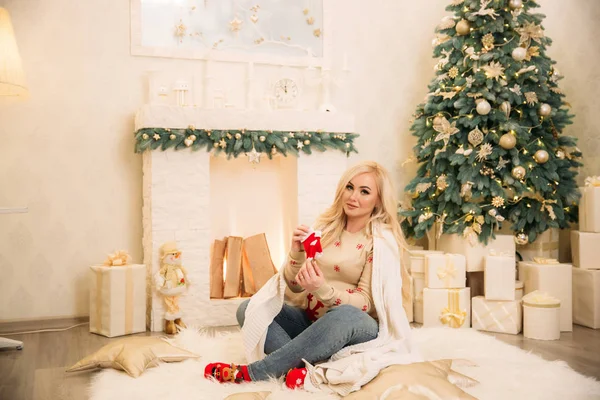 A futura mãe feliz senta-se junto à lareira da casa deles. Humor de Natal — Fotografia de Stock