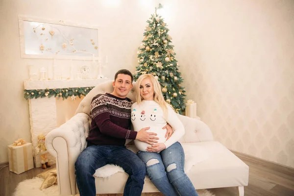 Yong fimily in mooie gebreide truien in kerstvakantie zit op de Bank tegenover kerstboom. Zwangere vrouw — Stockfoto