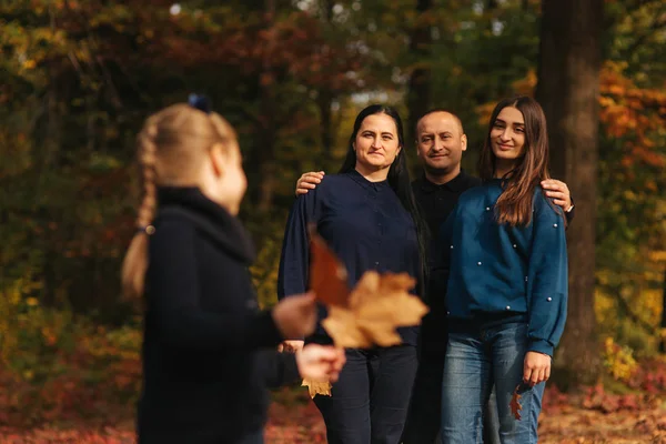 小女孩在森林里收集树叶。背景的妈妈, 爸爸和妹妹。年轻的家庭在秋天公园 — 图库照片
