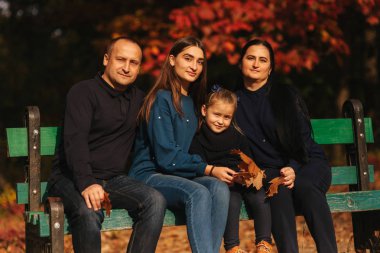 Anne baba ve iki kız kardeş güzel ve renkli parkta bankta oturur. Aile birlikte vakit geçirmek