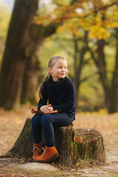 검은 옷에 어린 소녀는 그 루터 기에 앉아 이며 단풍 놀고. 금발 머리 소녀 — 스톡 사진