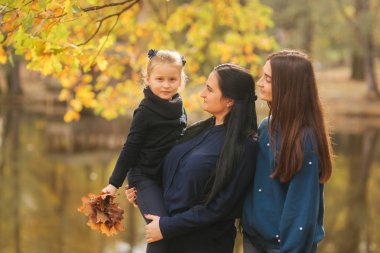 Anne ve iki kızı orada park eğlenmek. Genç kızı toplamak yaprakları ve gülümseme. Mutlu aile ormanda yürüyüş