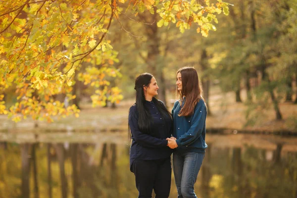 Mutter und Tochter stehen vor dem See im Park. Gelber Baum zur Herbstzeit — Stockfoto