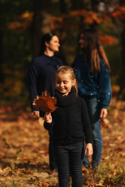 Kislány gyűjtsd hagyja az erdőben. Háttérben az apám anyám és a húgom. Őszi Park fiatal család — Stock Fotó