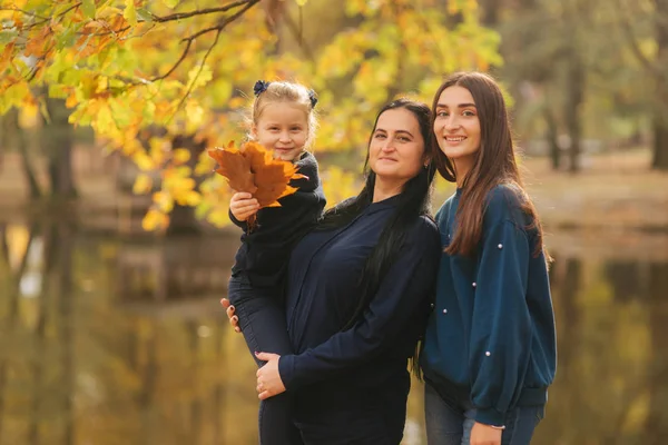 Mama și două fiice se distrează în ther park. Fiica cea mică colectează frunze și zâmbește. O familie fericită mergând în pădure — Fotografie, imagine de stoc