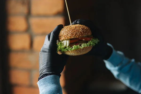 El hombre con guantes negros toma una hamburguesa en sus manos. Hamburguesa vegetariana con verduras. Alimentos frescos y saludables — Foto de Stock