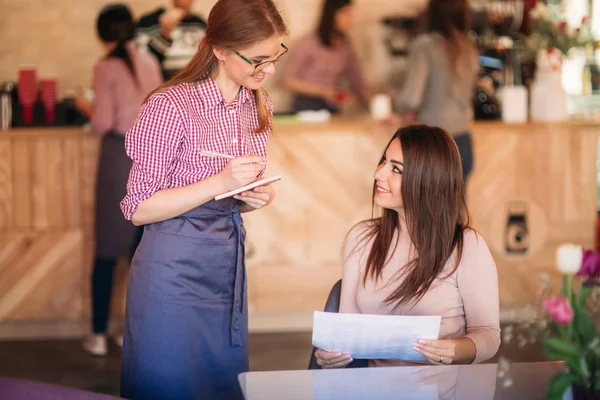Serveerster neemt bestelling van haar klant in een café — Stockfoto