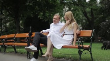 Güzel çift parkta bankta oturur. Sarı saçlı erkek ve kadın zaman togerther harcamak. Siyah şemsiye alırlar. Arka plan yeşil çimen