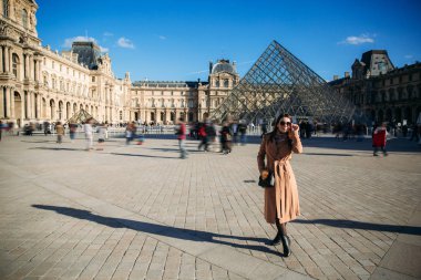 Bir genç kız bir kahverengi ceket ve eşarp şehir Paris arka plan üzerinde duruyor. Güneşli havalarda, turist sonbahar geldi