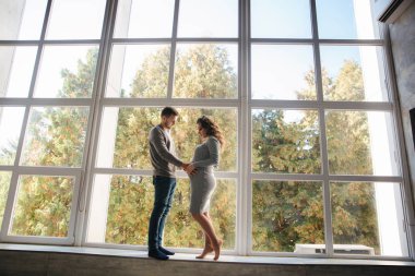 Güzel çift Studio büyük pencerenin önünde dur. Hamile kadın kocası ile