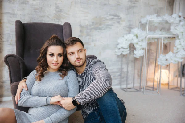 Pareja feliz se sienta cerca de la silla en su casa. Mujer embarazada con su amado marido. año nuevo — Foto de Stock