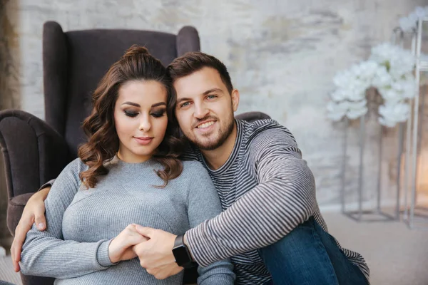 Glückliches Paar sitzt in der Nähe des Stuhls in ihrem Haus. schwangere Frau mit ihrem geliebten Mann. Neues Jahr — Stockfoto