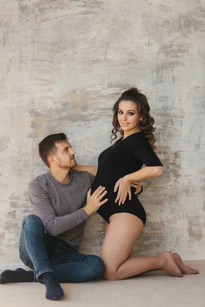 Feliz hombre puso su mano en el vientre de su esposa embarazada. Familia joven en el estudio. Un par de espera para un bebé — Foto de Stock