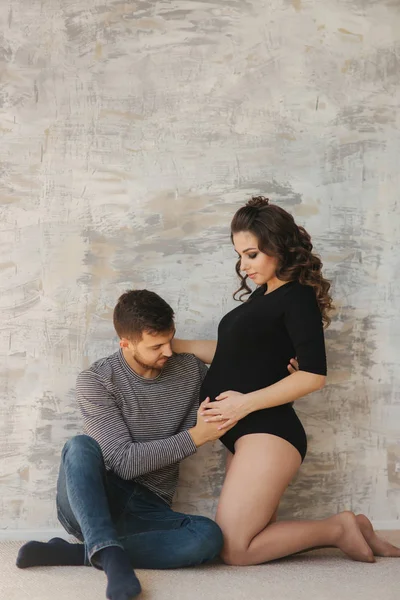 Feliz hombre puso su mano en el vientre de su esposa embarazada. Familia joven en el estudio. Un par de espera para un bebé —  Fotos de Stock