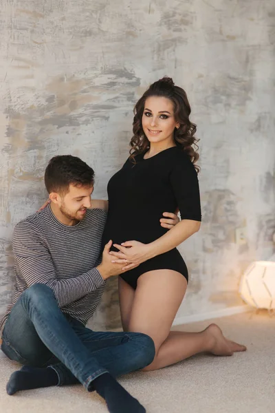 Feliz hombre puso su mano en el vientre de su esposa embarazada. Familia joven en el estudio. Un par de espera para un bebé —  Fotos de Stock