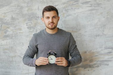 Studio gri arka plan üzerinde durabilen sakallı yakışıklı adam. O bir saat tutun. Bütün zamanı. Çizgili süveter giyen bir adam