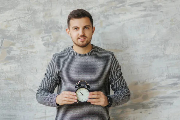 Studio gri arka plan üzerinde durabilen sakallı yakışıklı adam. O bir saat tutun. Bütün zamanı. Çizgili süveter giyen bir adam