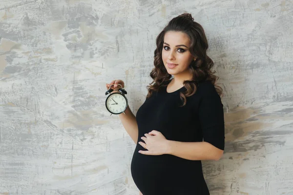 Ritratto di bella donna incinta in body nero. Tiene l'orologio tra le mani, suggerendo simbolicamente il tempo rimanente befour il bambino in nato — Foto Stock