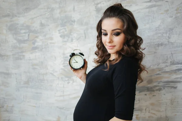 Беременная женщина держит в руках часы. Прекрасный портрет будущей матери. Женщина ждет ребенка, детка — стоковое фото
