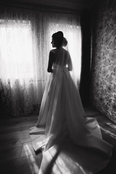 Belle jeune mariée debout devant la fenêtre dans sa chambre. Noir et blanc — Photo