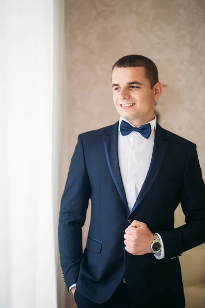 Handsome groom on a wedding day stand near the window — Stock Photo, Image
