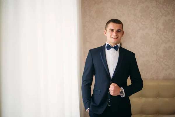 Handsome groom on a wedding day stand near the window — Stock Photo, Image