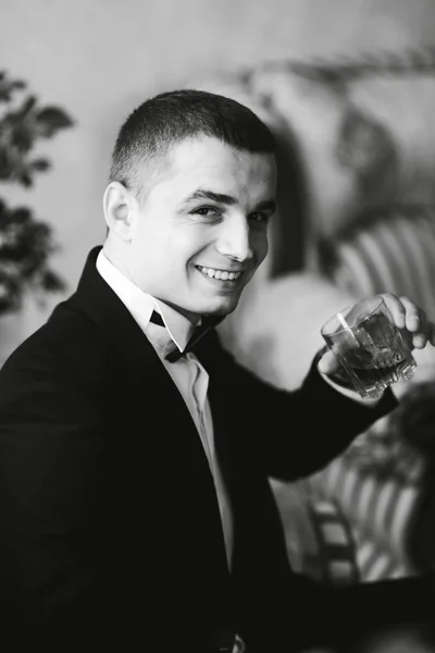 Schöner Mann im Hochzeitsanzug hält ein Glas Whiskey in der Hand — Stockfoto