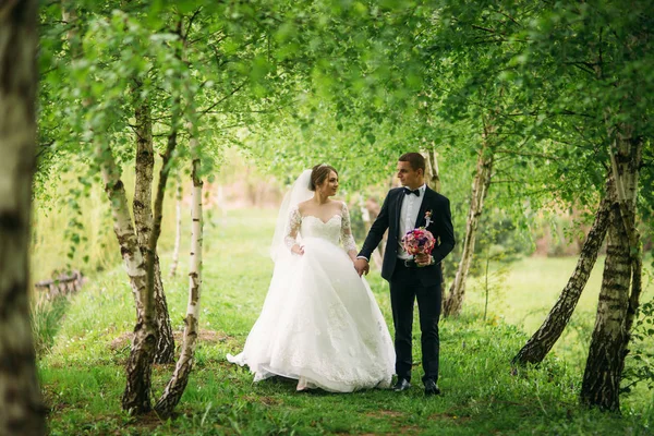 Das Brautpaar spaziert am Hochzeitstag durch den Park. Braut und Bräutigam beim Hochzeitstag — Stockfoto