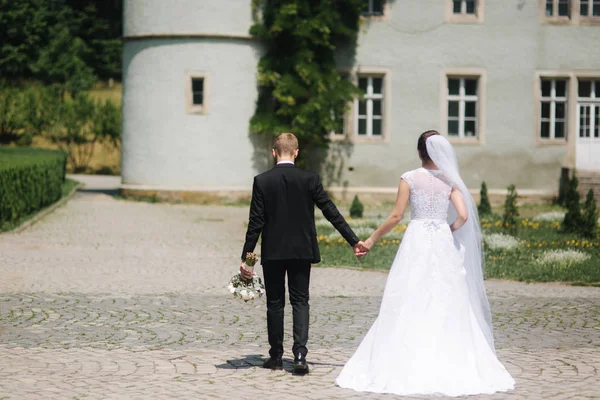 Жених и невеста идут через парк рядом с большим замком — стоковое фото