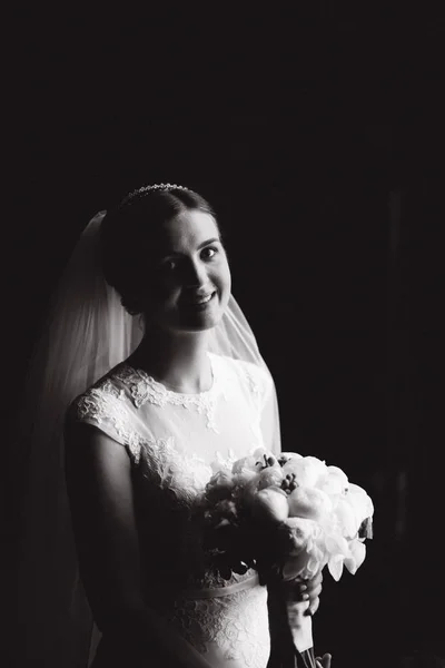 Black and white photo. Bride with bouquet stand near the window