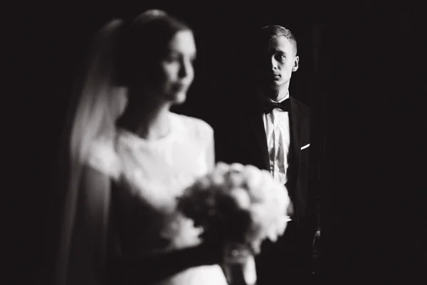 Foto em preto e branco. Noiva e noivo ficam perto da janela — Fotografia de Stock