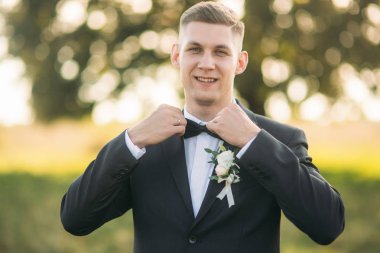 Damat papyon ayarlar. Yakışıklı adam alan büyük ağaç arka planda ortasında ayakta