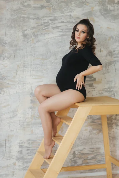 Těhotné Momana sedí na schodech. Model na sobě černou kombinézu. Položila mu ruku na břicho. Budoucí mamince — Stock fotografie