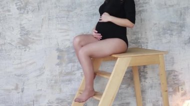 Hamile moman merdivenlerde otur. Model siyah elbise giymiş. Elini karnına koydu. Mutlu gelecekte anne