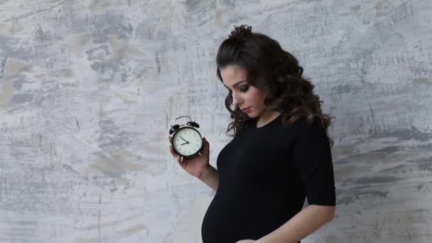 La giovane donna incinta tiene un orologio tra le mani. Bellissimo ritratto della futura madre. Donna in attesa di un bambino, baby — Video Stock