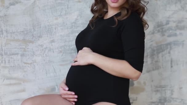 A mãe grávida senta-se nas escadas. Modelo vestido de macacão preto. Ela pôs a mão na barriga. Futura mãe feliz — Vídeo de Stock