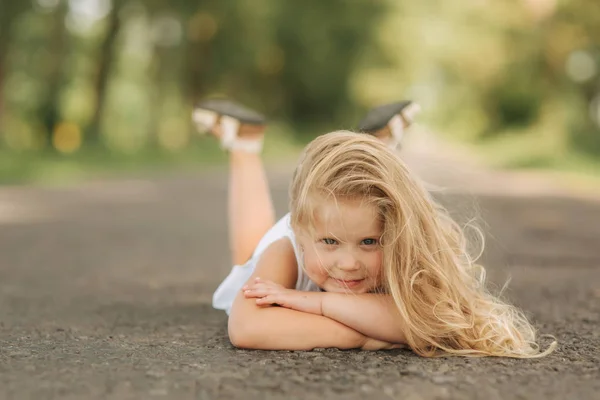 Маленькая девочка лежит на дороге рядом с большой аллеей — стоковое фото