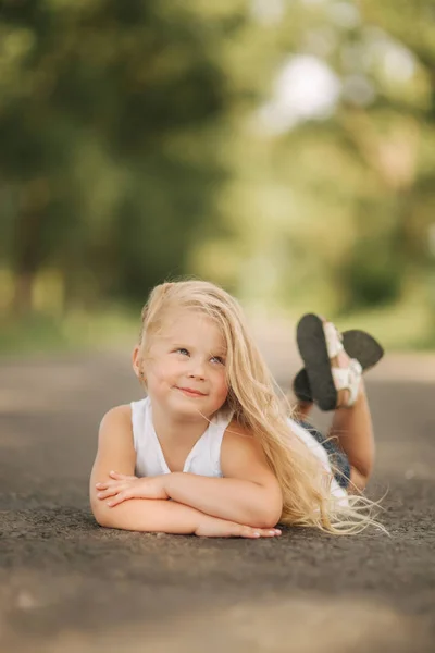 Маленькая девочка лежит на дороге рядом с большой аллеей — стоковое фото