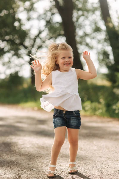 Een vrolijke schattig klein meisje met blond haar dansen en springt via het steegje op een warme zomerdag — Stockfoto