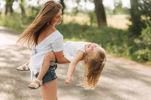 Malá dívka si hraje s mámou v parku v letním dni při západu slunce — Stock fotografie